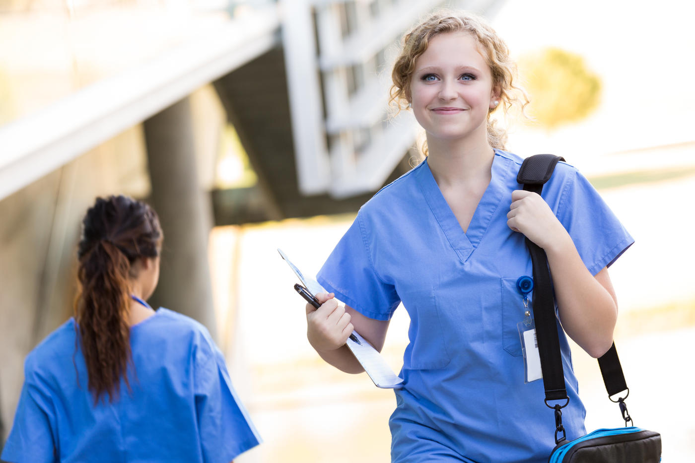 Smiling nurse with laptop bag walking outdoors